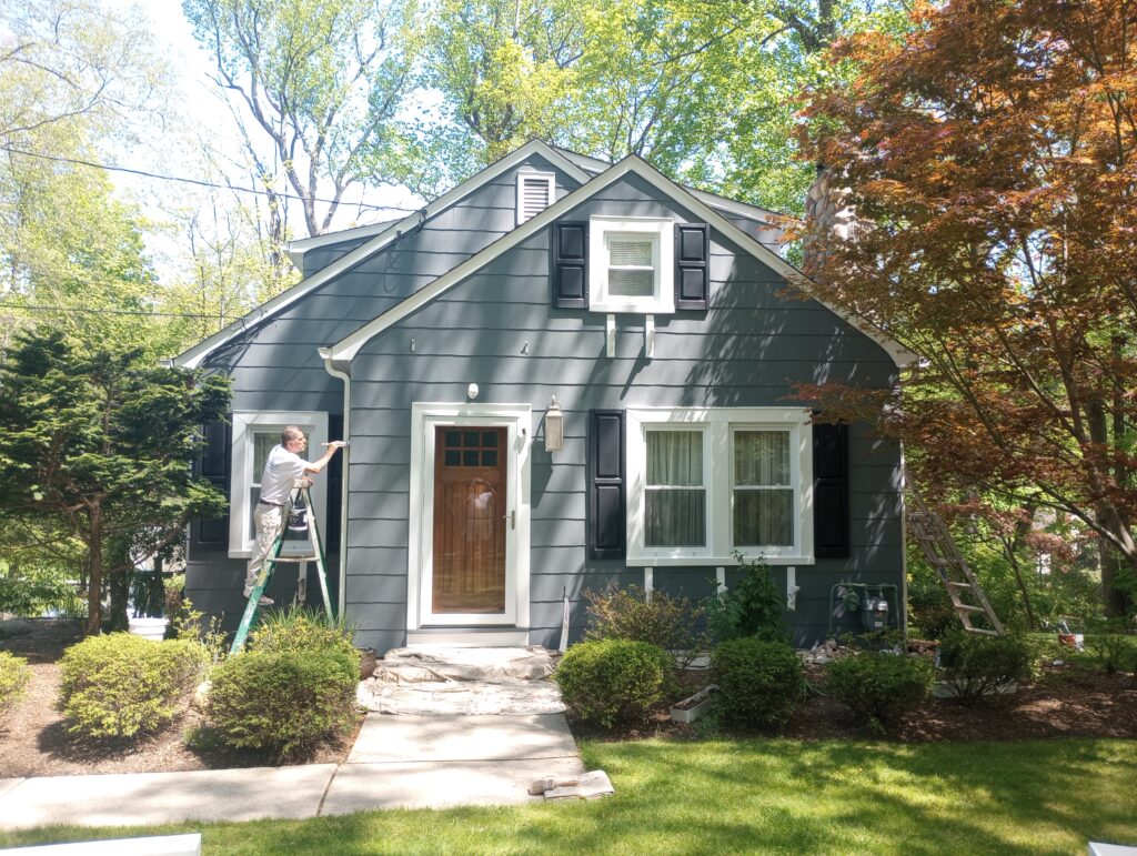Professional painter applying a dark gray exterior finish to a home in Upper Saddle River, NJ