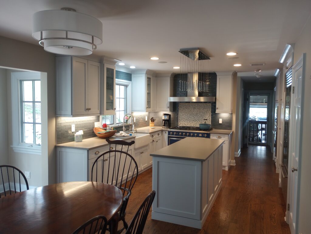A professionally painted luxury kitchen interior in Mahwah, New Jersey, showcasing flawlessly coated walls, crisp white window frame moldings, and seamless ceiling trim painting framing a modern island, tile backsplash, and dark wood flooring.