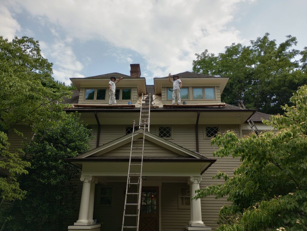 Professional house painters from Perfection Plus Painting wearing white uniforms working on ladders and scaffolding to paint the upper trim, dormers, and siding of a historic multi-story home in Ho-Ho-Kus, New Jersey.